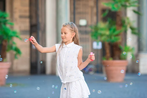 Adorable niña soplando burbujas de jabón en la ciudad europea. Retrato de niño caucásico disfrutar de vacaciones de verano en Italia —  Fotos de Stock
