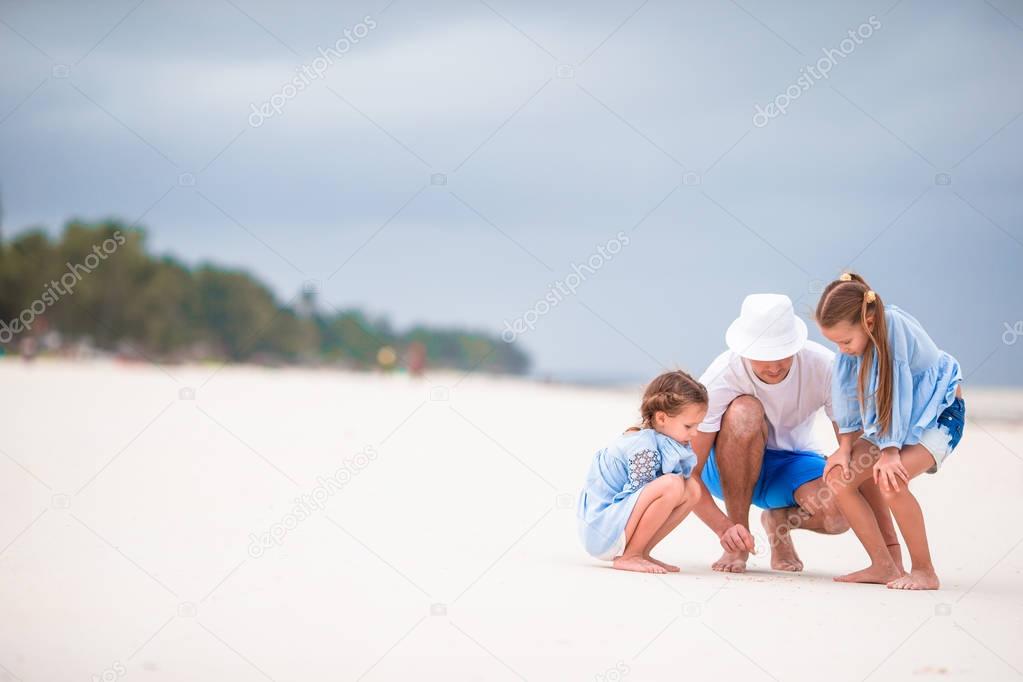 Young family enjoying beach summer vacation. Kids and dad find something on the sand