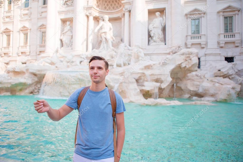 Happy man trowing coins at Trevi Fountain, Rome, Italy for good luck. Caucasian guy making a wish to come back.