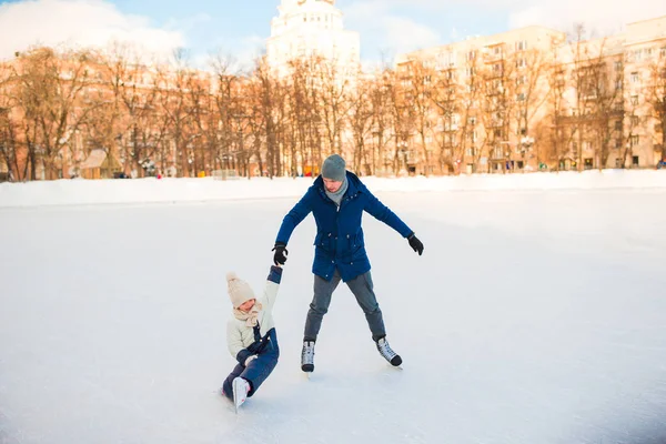 Lilla bedårande flicka med far lära sig att åka skridskor på ishallen — Stockfoto