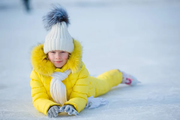 Маленька чарівна дівчинка лежить на льоду з ковзанами після осені — стокове фото