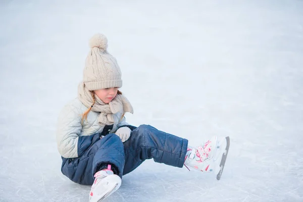 Kleines entzückendes Mädchen sitzt nach Sturz mit Schlittschuhen auf dem Eis — Stockfoto