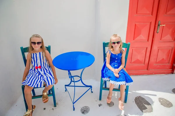Two girls in blue dresses sitting in outdoor cafe on street of typical greek village on Mykonos Island, Greece — Stock Photo, Image