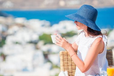 Güzel bir kadın harika manzaralı bir kafede kahvaltı yapıyor. Kız sabahın köründe sıcak kahvesinin tadını çıkarıyor.