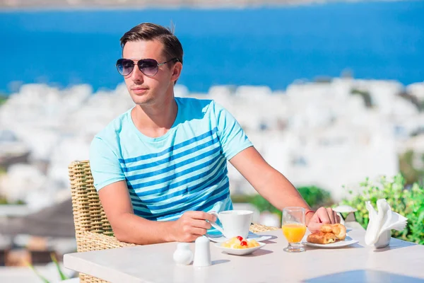 Ung kille att ha frukost på uteservering med fantastisk utsikt över staden Mykonos. Man dricka kaffe på luxury hotel terrass — Stockfoto