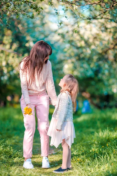 Adorable niña con madre joven en el jardín de manzanas en flor en el hermoso día de primavera —  Fotos de Stock