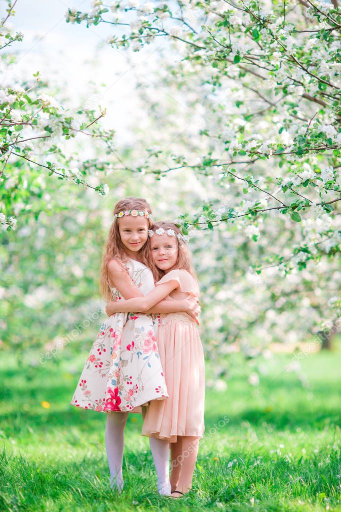 Adorable little girls in blooming cherry tree garden on spring day