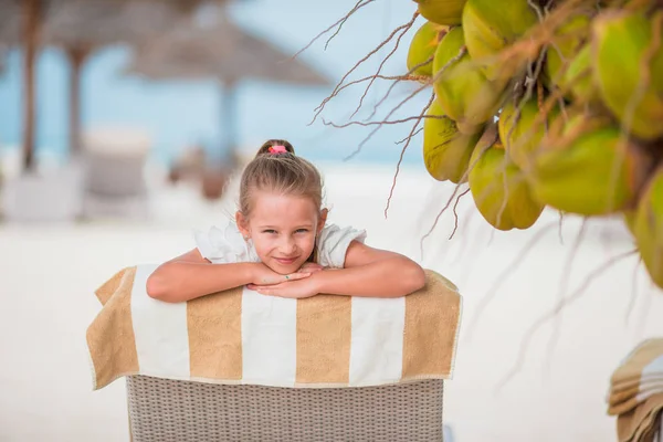 Adorable girl on lounger at tropical exotic beach under big coconuts — Stock Photo, Image