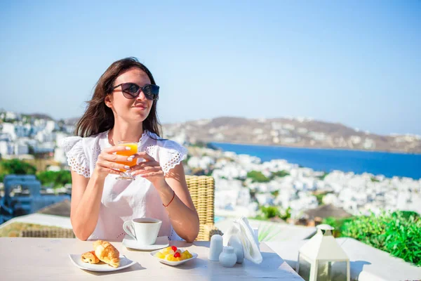 Turist kadın kahvaltı kahve ile Mykonos şehri üzerinde muhteşem manzaralı açık kafe. — Stok fotoğraf