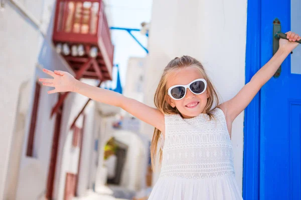 Krásná dívka se bavit ve starých uličkách na Mykonos. Kid chůze typické řecké vesnice s bílými stěnami a barevnými dveřmi — Stock fotografie