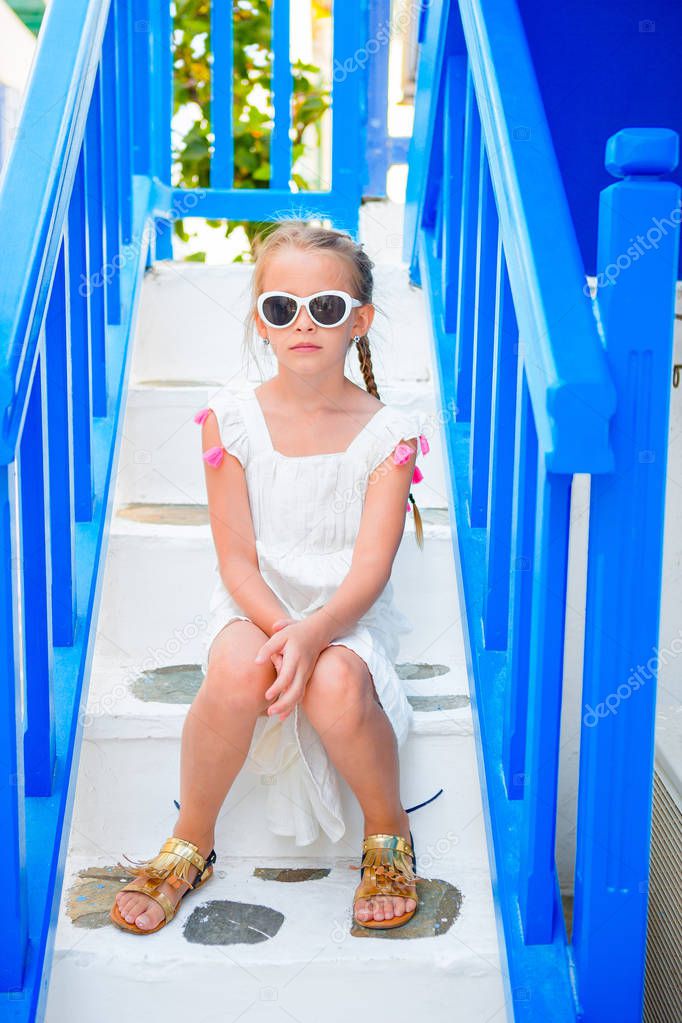 Adorable little girl on the steps at street of typical greek traditional village on Mykonos Island, in Greece