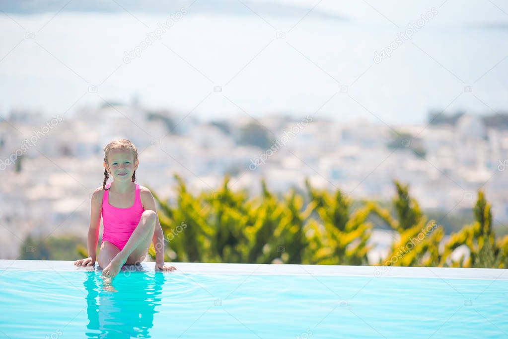 Adorable little girl on the edge of outdoor swimming pool with beautiful view