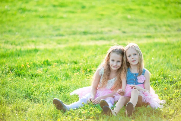 Urocze dziewczynki na dzień wiosny na zewnątrz siedząc na trawie — Zdjęcie stockowe