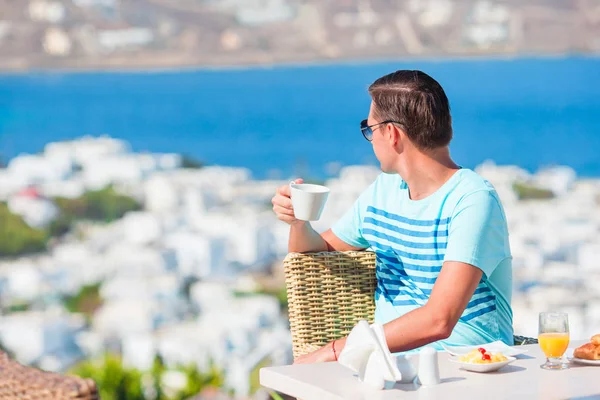 Chico joven en el desayuno en la cafetería al aire libre con una vista increíble en la ciudad de Mykonos . —  Fotos de Stock
