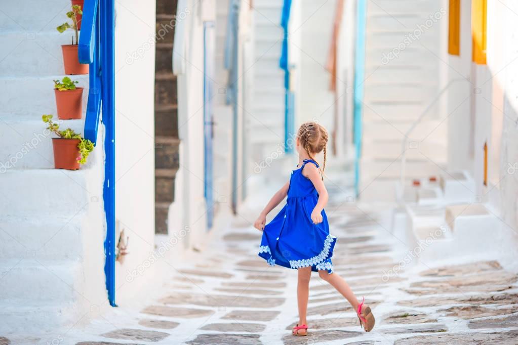 Little girl in blue dress outdoors. Kid dancing at street of typical greek traditional village on Mykonos