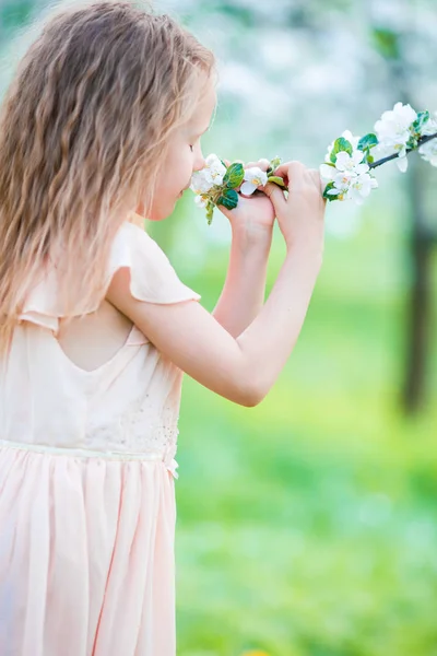 Pequena menina bonita desfrutando cheiro de árvore de maçã florescente em um jardim de primavera florido — Fotografia de Stock
