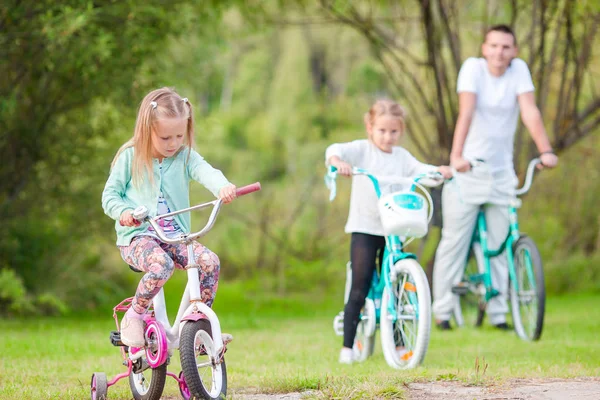 Adorable girls and happy dad biking at summer warm day. Young active family ride on bicycles — Stock Photo, Image