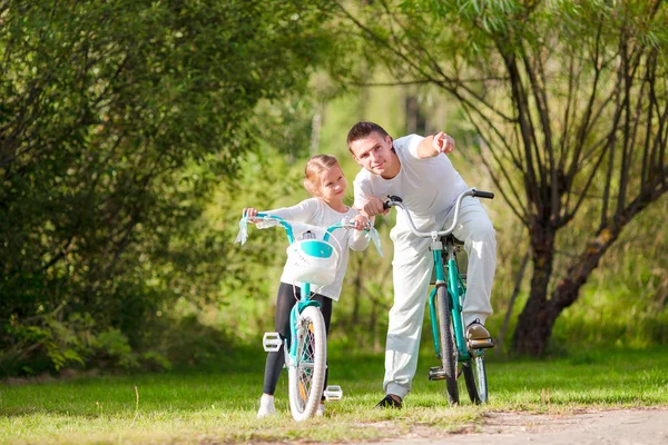 Unga far och liten flicka cykling på sommaren varm dag. Ung aktiv familj rida på cyklar — Stockfoto