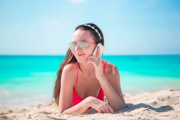 Giovane donna con cellulare sdraiata sulla spiaggia bianca — Foto Stock
