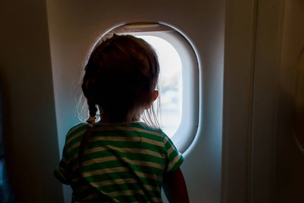 Kleines Mädchen blickt aus dem Flugzeugfenster. entzückendes kleines Kind, das im Flugzeug reist — Stockfoto