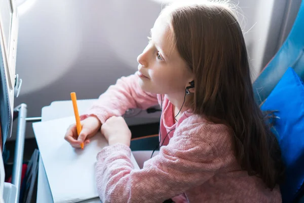 Sevimli küçük kız bir uçakla seyahat. Pencere oturmak renkli kalemler ile evlat çizim resim — Stok fotoğraf
