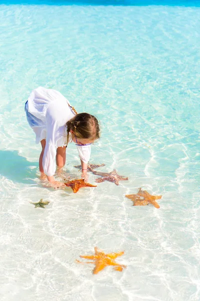 Adorable niña con estrellas de mar en el agua en el agua clara —  Fotos de Stock