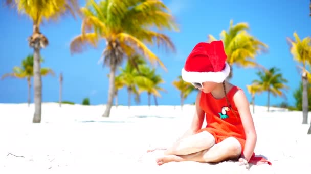 Kleines entzückendes Mädchen mit roter Weihnachtsmütze am tropischen Strand an den Weihnachtsfeiertagen — Stockvideo