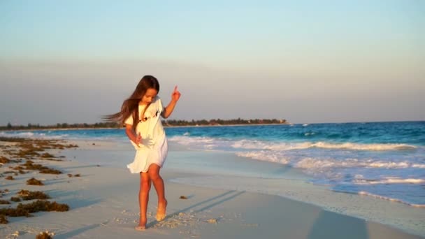 Αξιολάτρευτο ευτυχισμένη μικρό κορίτσι στην παραλία με λευκή κατά το ηλιοβασίλεμα. Χαριτωμένο παιδί χορού στην τροπική παραλία βίντεο αργής κίνησης — Αρχείο Βίντεο