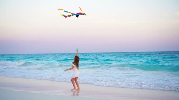 Entzückendes kleines Mädchen mit fliegendem Drachen am tropischen Strand. Kinder spielen am Meeresufer mit schönem Sonnenuntergang — Stockvideo