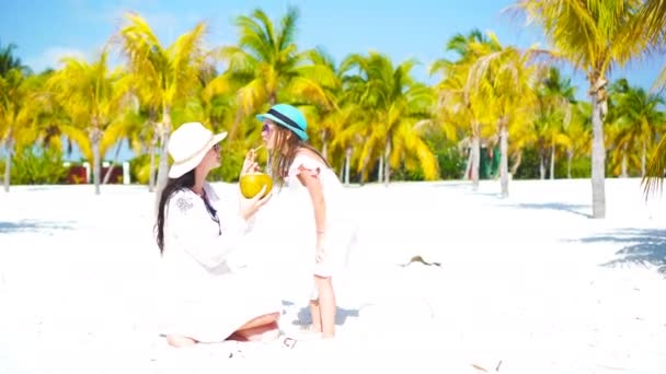 Kleines Kind und junge Mutter mit Kokosmilch am exotischen Strand. süßes Mädchen trinkt gesunde Kokosmilch in einem Palmenhain — Stockvideo