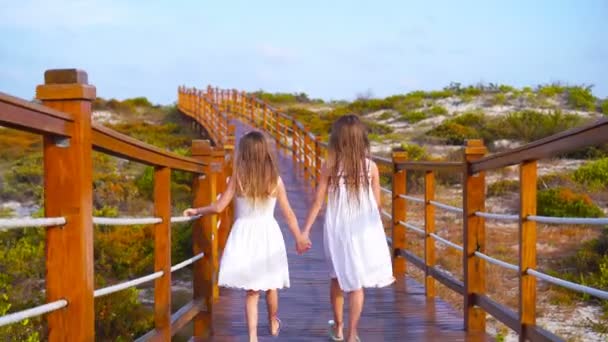 Meninas adoráveis em uma ponte de madeira a caminho de uma praia tropical branca . — Vídeo de Stock