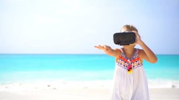 Cute little child girl using VR virtual reality goggles. Adorable girl look into the virtual glasses on white beach — Stock Video