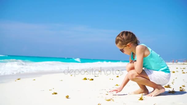Чарівна маленька дівчинка на пляжі під час літніх канікул малює на піску — стокове відео
