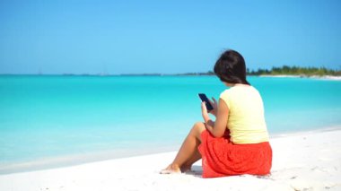 Genç bir kadın tropik plaj tatilinde telefon kullanıyor. Akıllı telefon kullanan turist.