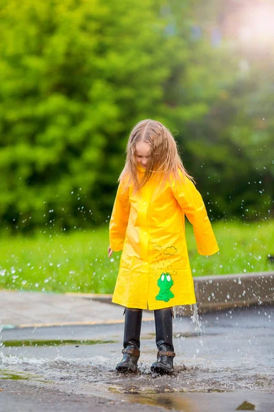 Kleines Mädchen in Regenmantel und Stiefeln, das draußen im Regen spielt — Stockfoto