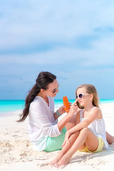 Молодая мама наносит крем для загара дочери на нос на пляже. Концепция защиты от ультрафиолетового излучения — стоковое фото