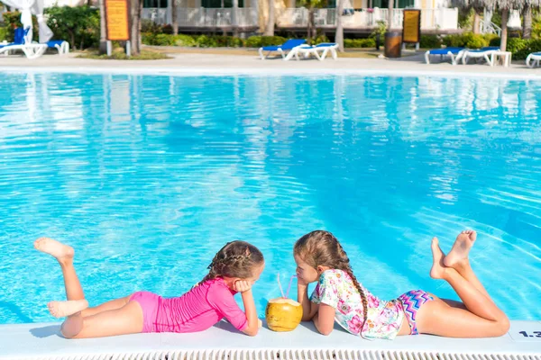 Little girls in outdoor swimming pool drink coconut milk — Stock Photo, Image