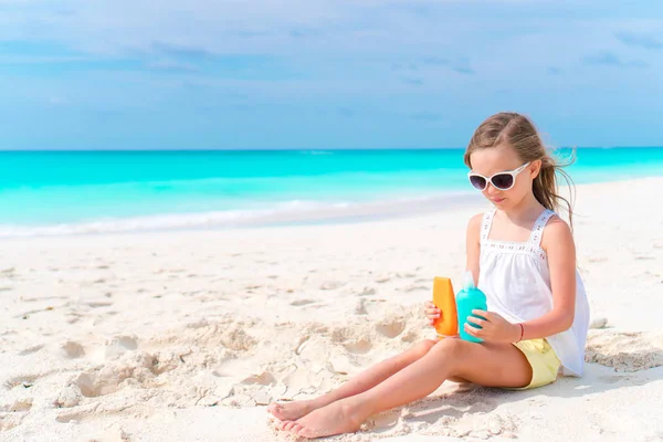 Pequena menina adorável com garrafa de creme solar na praia — Fotografia de Stock