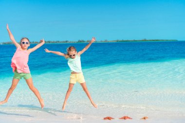 Sevimli küçük kızlar eğleniyor kum üzerinde denizyıldızı tam sahilde