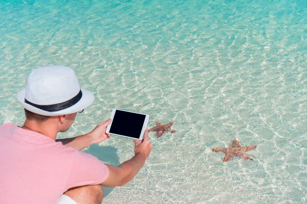 Młody człowiek z laptopa na tle turkus oceanu na tropikalnej plaży — Zdjęcie stockowe