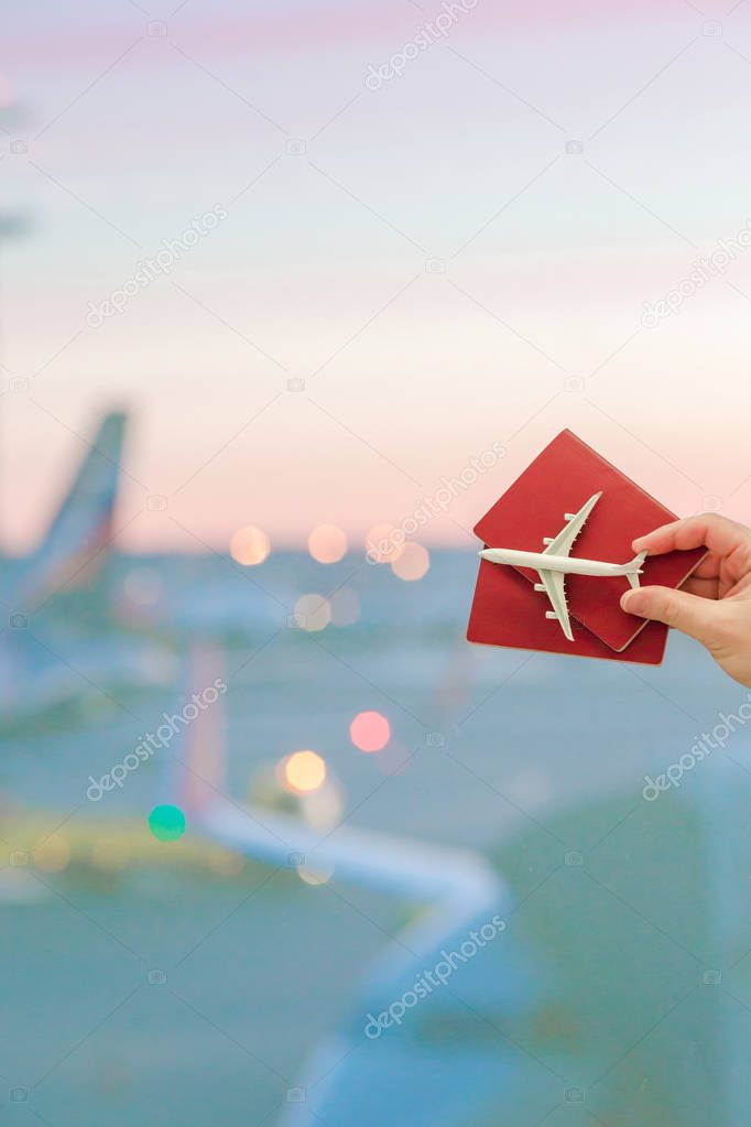 Closeup hand holding an airplane model toy and passports at the airport background big window