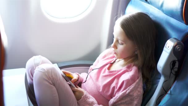 Adorable niñita viajando en un avión. Lindo niño con portátil cerca de la ventana en avión — Vídeos de Stock