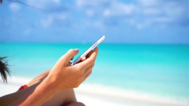 Genç bir kadın tropik plaj tatilinde telefon kullanıyor. Kapalı cep telefonu akıllı telefon.