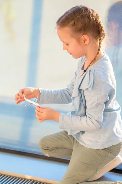 Suloinen pieni tyttö leikkii pieni malli lentokone lentokentällä odottaa lennolle — kuvapankkivalokuva