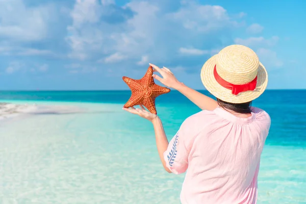 Young girl in hat holding giant red starfish on white beach in the nature reserve — Stock Photo, Image
