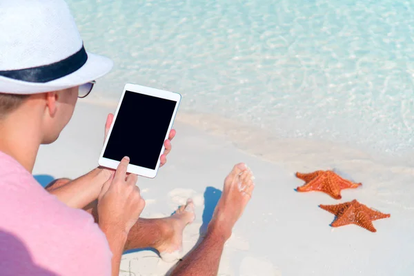 Jonge man met de laptop op de achtergrond van turkoois Oceaan op tropisch strand nemen een foto van starfish in natuurreservaat — Stockfoto