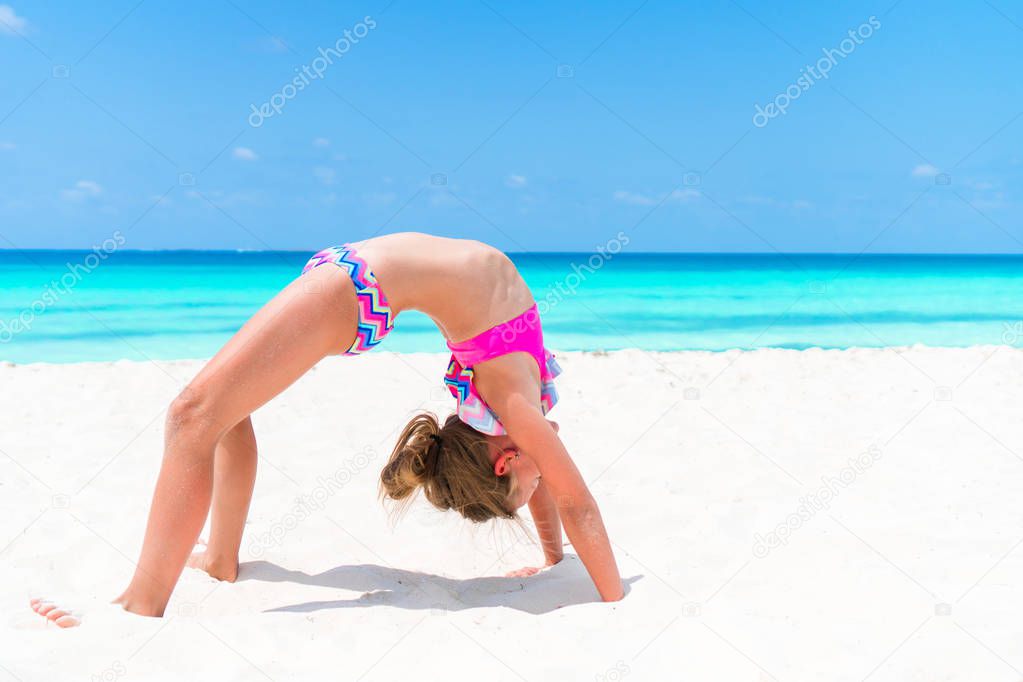 Active little girl at beach having a lot of fun. Sporty kid makes sport exercises on the seashore
