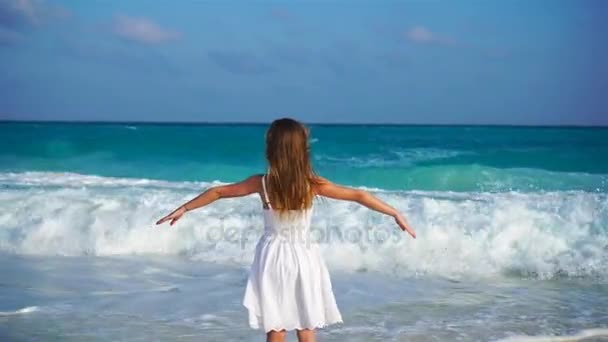 Adorable niña feliz en la playa blanca mirando al océano. Mar ruidoso y un niño pequeño y lindo — Vídeo de stock