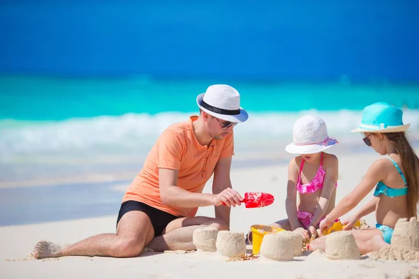 Отец и маленькие дочери строят замок из песка на тропическом пляже — стоковое фото