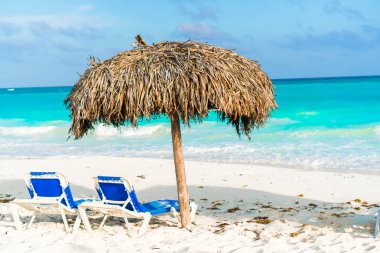 Plaj güneşlikleri ve beyaz sahilde şemsiye.